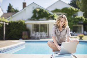 Woman using laptop on diving board at poolside
