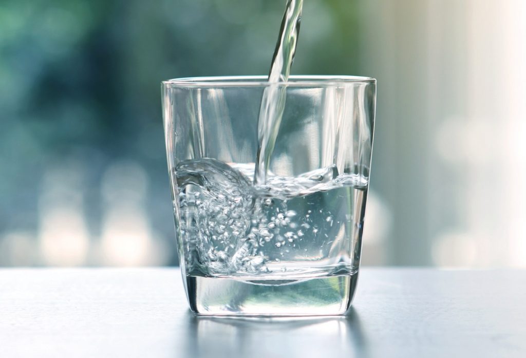 Close up the pouring purified fresh drink water from the bottle on table in living room