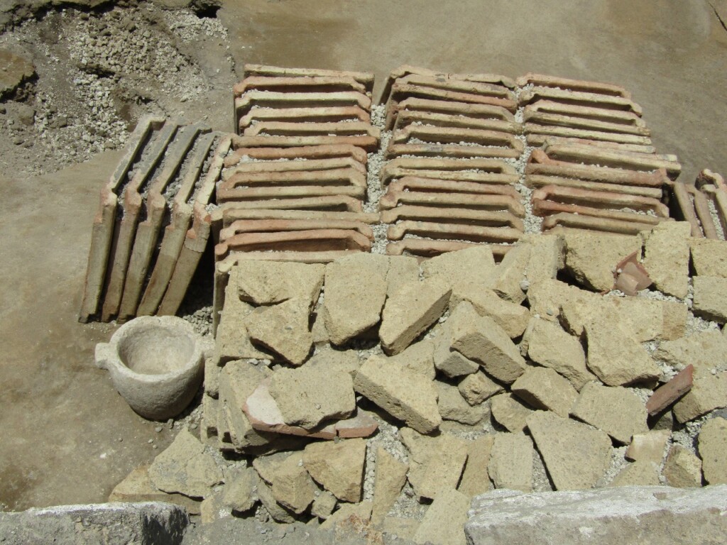 File di tegole e cataste di blocchetti in tufo giallo dall'atrio del panificio Regio IX - 2